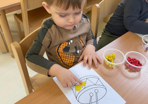Chłopczyk wykleja rysunek bębna kawałkami żółtej plasteliny.