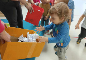 Szymon wkłada do pudełka oklejonego pomarańczową bibułą, zebrane przez siebie z podłogi papierowe śnieżki.