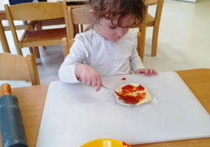 Dziewczynka smaruje passatą pomidorową swoją pizzę.