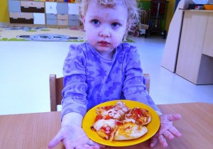 Dziewczynka pozuje do zdjęcia z upieczoną pizzą.