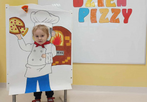 Daniel pozuje do zdjęcia na wykonanej własnoręcznie ściance przedstawiającej Piekarza z pizzą.