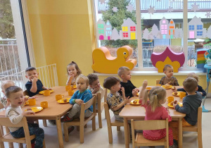 Zdjęcie dzieci z grupy Pszczółki siedzących przy stoliczku podczas kosztowania otrzymanych słodkości w postaci przepysznych pączuszków.