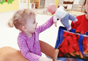 Dziewczynka wyjmuje z torby zakupowej lalkę.