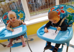 Dzieci siedzace w fotelikach malują obrazki.