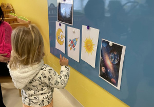 Mała dziewczynka przygląda się obrazkom przyklejonym do tablicy.