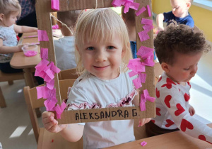 Aleksandra pozuje do zdjęcia z ozdobioną przez siebie ramką różowymi kawałkami bibuły.
