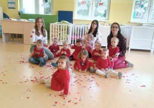 Zdjęcie dzieci i opiekunek w Dniu Walentynek siedzących na podłodze przed zabawą z serduszkowym konfetti.