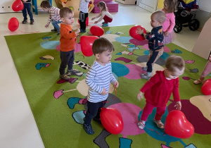 Dzieci z grupy Żabki podczas zabawy czerwonymi balonami w kształcie serca.