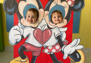 Chłopiec i dziewczynka ustawieni do wspólnego zdjęcia na sciance z Myszką Mickey i Minnie.