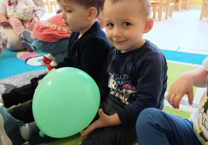 Trzymający w dłoni zielony balonik Leon uśmiecha się do zdjęcia podczas zajęć.