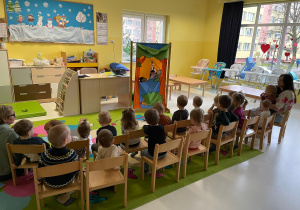 Dzieci siedzące na krzesełkach i oglądające przedstawienie w formie teatrzyku.