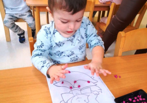 Chłopczyk nakleja różowe kuleczki plasteliny na szablon wróżki.