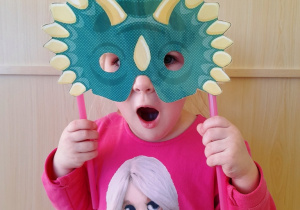 Dziewczynka pozuje do zdjęcia w Dzień Dinozaura z maską na twarzy.