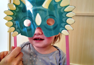 Mała dziewczynka z maską dinozaura na twarzy.