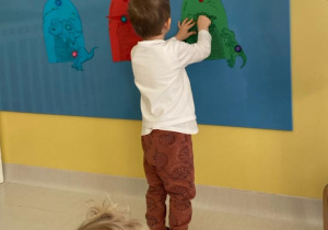 Jeden z chłopców przykleja dinozaura przy jaskini w tym samym kolorze.