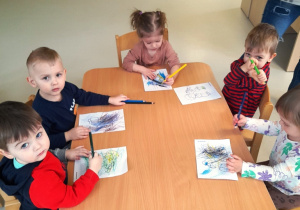 Dzieci siedzace przy stole malują obrazki.