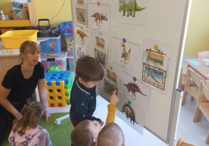 Dzieci wskazują na obrazki dinozaurów wiszące na tablicy.