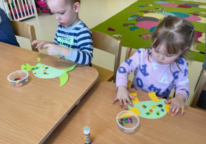 Dwoje dzieci wykleja swoje papierowe dinozaury plasteliną.