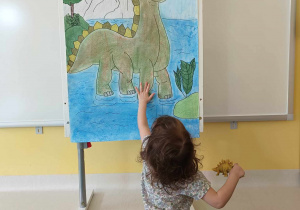 Barbara dotyka dłonią pomalowanego za pomocą pasteli dinozaura.