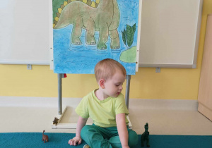 Zdjęcie Szymona przyglądającego się ustawionym obok niego figurkom dinozaurów.