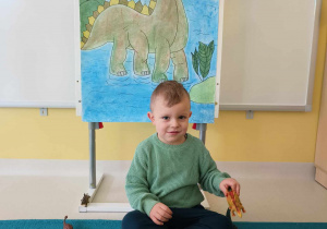 Uśmiechnięty Hubert pozuje do zdjęcia trzymając w dłoni żółtego dinozaura.