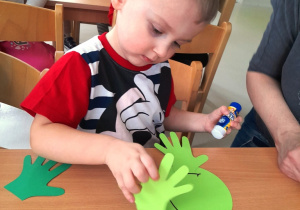 Chłopiec przykleja żabce z papieru łapkę.