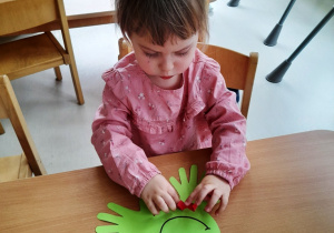Dziewczynka przykleja papierowy, czerwony język do szablonu żaby.