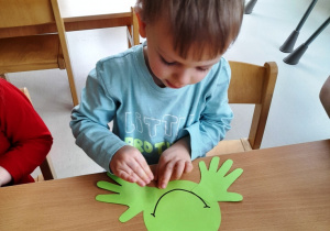 Chłopczyk dokleja szablon łapki do zielonej żabki.