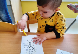 Chłopiec koloruje żółtą kredką obrazek.