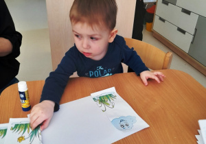 Chłopiec nakleja obrazek na kartkę.