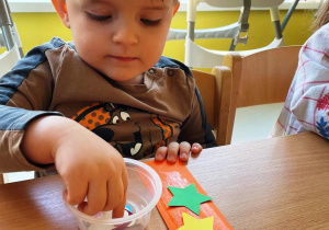 Chłopiec dekoruje ozobami z papieru swoją pomarańczową zakładkę.