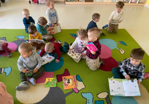 Maluchy siedząc na dywanie przeglądają ilustracje w książkach.