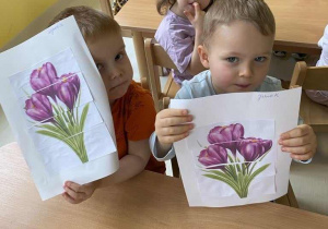 Wojciech i Jakub pokazują opiekunce ułożone i przyklejone na kartkę A5 puzzle przedstawiające wiosenne fioletowe krokusy.