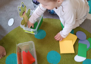 Dawid wkłada do pudełeczka z obrazkiem żabki zieloną karteczkę w kształcie prostokąta.