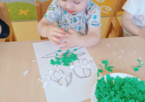 Mikołaj przykleja na swój obrazek zieloną pociętą bibułę.