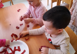 Dwoje dzieci przykleja bibułę na talerz.