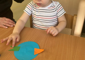 Chłopiec dokleja ogonek do ptaszka z papieru.