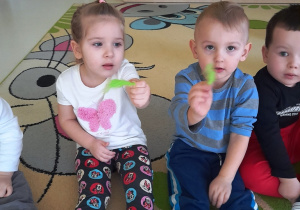 Zdjęcie dziewczynki i chłopca trzymających w dłoniach zielone piórka.