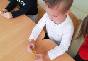 Zdjęcie chłopca robiącego świeczkę z plastra wosku pszczelego i sznurka.