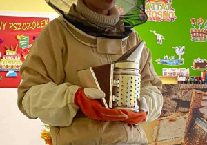 Pani Pszczelarka pokazuje dzieciom i opiekunkom trzymany w dłoniach podkurzacz pszczelarski.