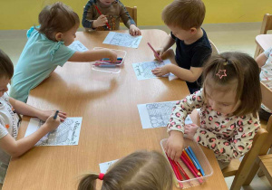 Zdjęcie dzieci wybierających z plastikowych prostokątnych pojemniczków kolorowe kredki.
