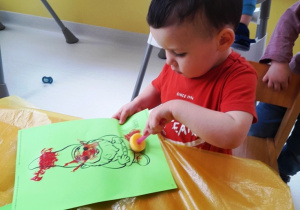 Chłopiec stempluje gąbką umoczoną w czerwonej farbie szablon krasnala.