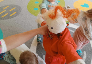 Tobiasz próbuje samodzielnie przyczepić Marzannie włosy z pomarańczowo - kremowego sizalowego sianka.