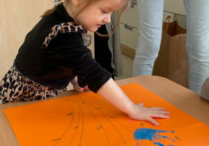 Dziewczynka odciskająca dłoń pomalowną farbą na plakacie.