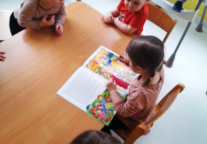 Maluchy przy wspólnym stole oglądające książeczkę o krasnalach.