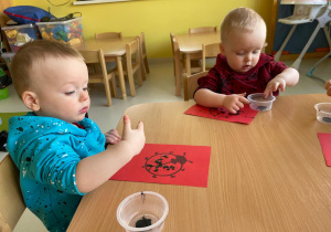 Dwoje dzieci przy stoliku wykleja plasteliną biedronki.