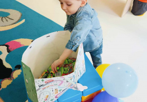 Zdjęcie Tymoteusza wyciągającego z urodzinowej torby pierwszy musik dla dzieci z grupy.