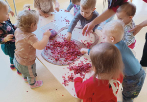 Opiekunka pomaga dzieciom ozdobić szablon koszyczka brązową bibułą.