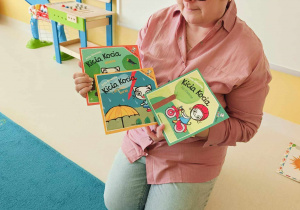 Opiekunka pokazuje dzieciom przygotowane na zajęcia książeczki z przygodami Kici Koci.