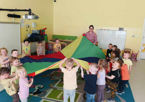 Zdjęcie dzieci bawiących się razem z opiekunką kolorową chustą animacyjną.